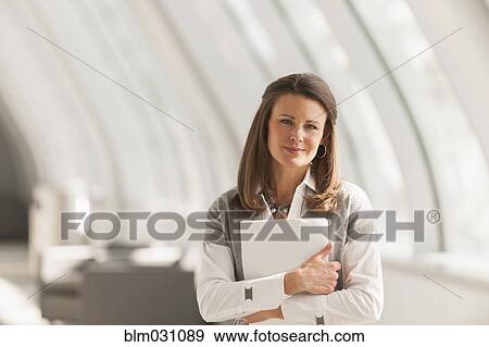 Stock Photo - Caucasian businesswoman carrying papers in lobby. Fotosearch