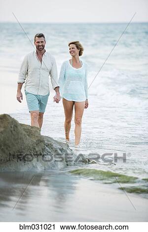 Stock Image - Caucasian couple holding hands on beach. Fotosearch