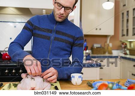 Stock Photo - Caucasian man cooking chicken in kitchen. Fotosearch