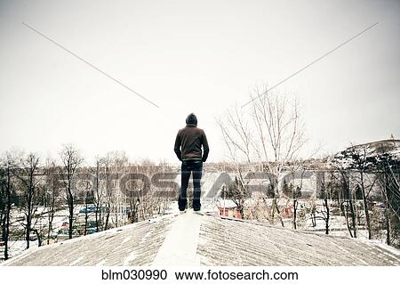 Stock Image - Caucasian man standing on snowy roof. Fotosearch