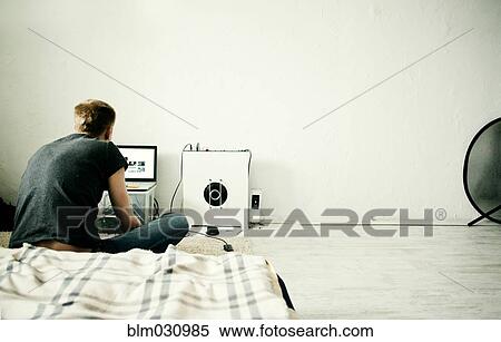 Stock Photography - Caucasian man using laptop in bedroom. Fotosearch