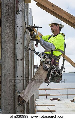 Stock Photo - Caucasian worker hammering nails at construction site. Fotosearch