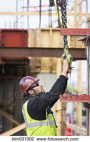 Stock Image - Caucasian worker holding hook at construction site. Fotosearch