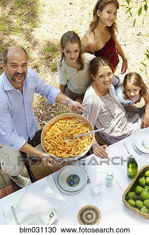 Stock Image - Family eating together at table outdoors. Fotosearch