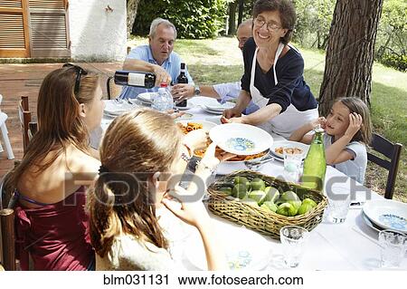 Stock Image - Family eating together at table outdoors. Fotosearch