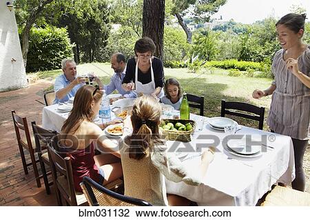 Stock Image - Family eating together at table outdoors. Fotosearch