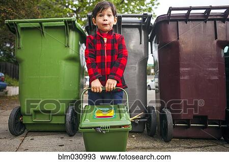 Stock Image - Mixed race boy carrying compost bin outdoors. Fotosearch