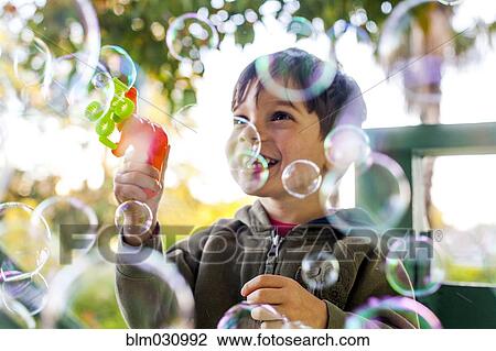 Stock Image - Mixed race boy playing with bubbles outdoors. Fotosearch