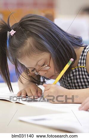 Stock Image - Mixed race Down syndrome student writing in workbook. Fotosearch