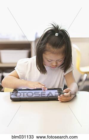 Stock Image - Mixed race Down syndrome student using tablet computer in classroom. Fotosearch