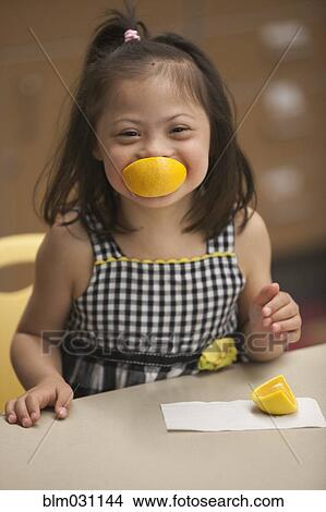 Picture - Mixed race girl with Down syndrome eating fruit. Fotosearch