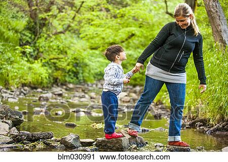 Stock Image - Mother and son exploring rocky creek. Fotosearch