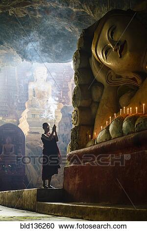 Stock Image - Asian monk lighting incense in temple. Fotosearch