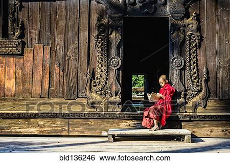 Stock Photograph - Asian monk reading by ornate doorway to temple. Fotosearch