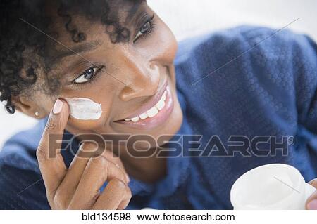 Stock Photo - Black woman applying lotion to her cheek. Fotosearch