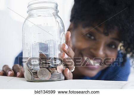 Stock Photo - Black woman saving coins in jar. Fotosearch