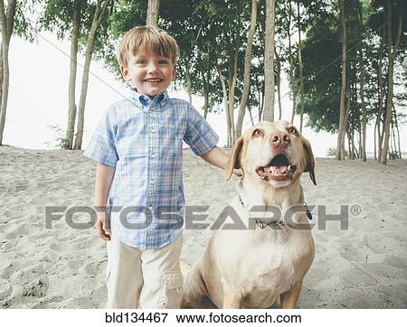 Stock Photo - Boy petting dog on wooded beach. Fotosearch
