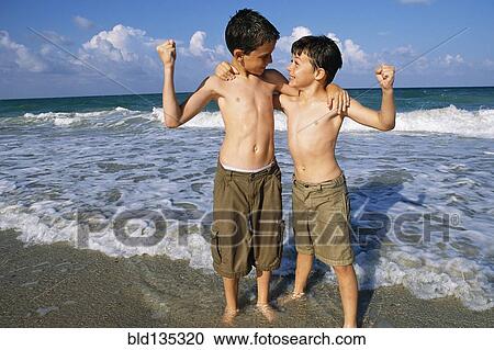 Stock Image - Boys flexing their muscles on beach. Fotosearch