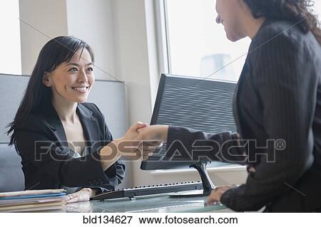 Stock Photo - Businesswomen shaking hands in office. Fotosearch