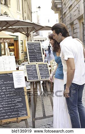 Stock Photo - Caucasian couple reading menus on city street. Fotosearch