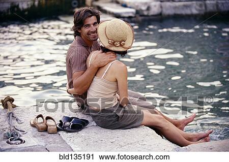Stock Image - Caucasian couple sitting together by canal. Fotosearch