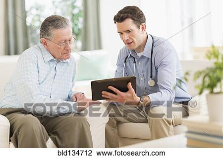 Stock Image - Caucasian doctor and patient using digital tablet at home. Fotosearch