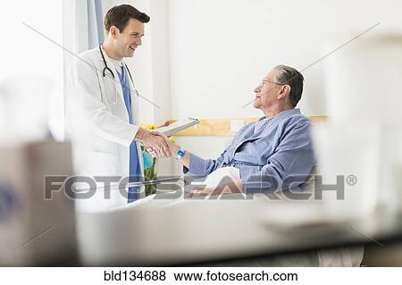 Stock Photo - Caucasian doctor shaking hands with Senior patient in hospital. Fotosearch