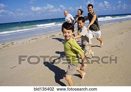 Stock Image - Caucasian family running on beach. Fotosearch