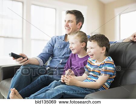 Stock Photo - Caucasian father and children watching television on sofa. Fotosearch