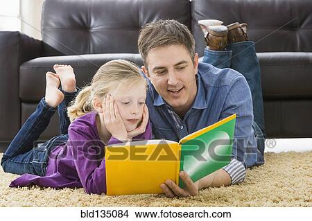 Picture - Caucasian father and daughter reading in living room. Fotosearch