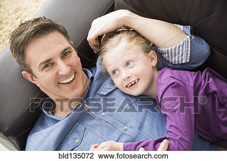 Stock Image - Caucasian father and daughter relaxing on sofa. Fotosearch