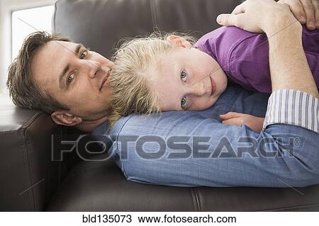 Stock Image - Caucasian father and daughter relaxing on sofa. Fotosearch