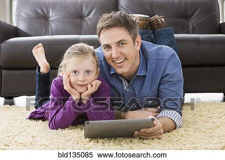 Stock Photography - Caucasian father and daughter using tablet computer in living room. Fotosearch
