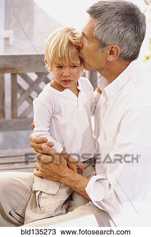 Stock Image - Caucasian father kissing crying son outdoors. Fotosearch