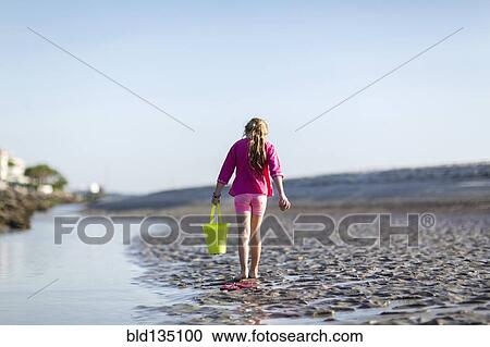 Stock Image - Caucasian girl carrying bucket on beach. Fotosearch