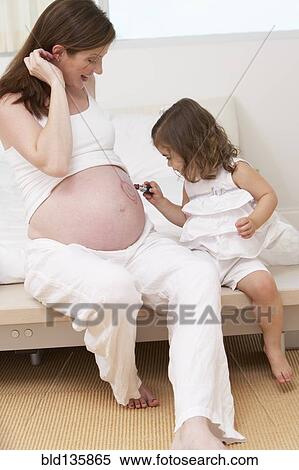 Stock Photography - Caucasian girl drawing on mother's pregnant belly. Fotosearch