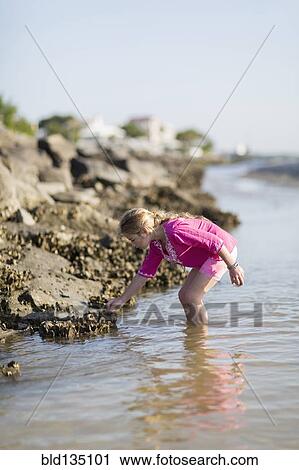 Stock Image - Caucasian girl exploring on rocky beach. Fotosearch