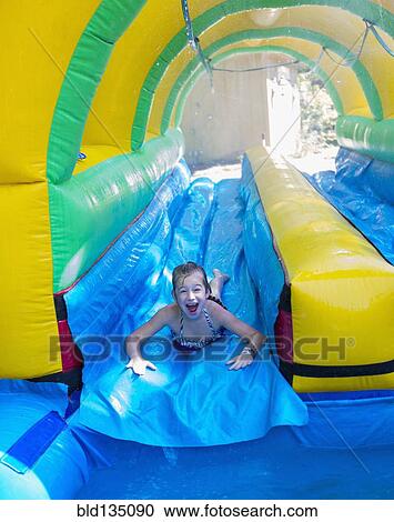 Stock Image - Caucasian girl laughing on water slide. Fotosearch