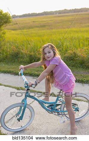 Picture - Caucasian girl riding bicycle on rural street. Fotosearch