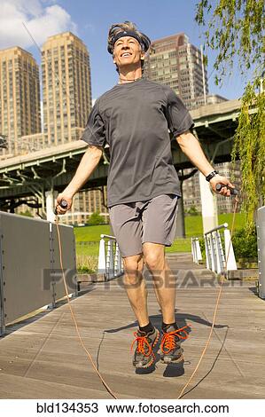 Stock Image - Caucasian man jumping rope in urban park. Fotosearch
