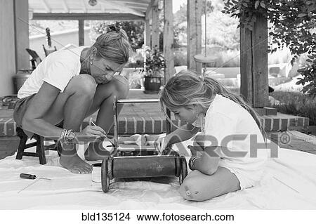 Picture - Caucasian mother and daughter painting toy on porch. Fotosearch
