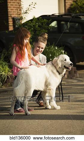 Stock Image - Caucasian mother and daughter petting dog on suburban street. Fotosearch