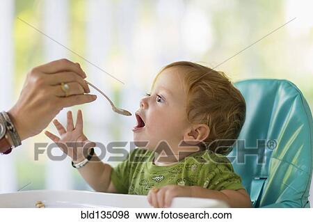 Caucasian mother feeding baby in high chair View Large Photo Image Stock Photo - Caucasian mother feeding baby in high chair. Fotosearch