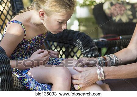 Stock Image - Caucasian mother putting bandage on daughter's knee. Fotosearch