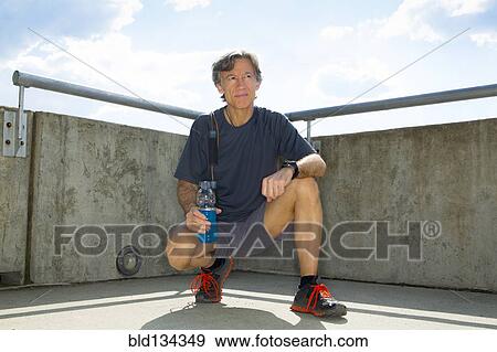 Stock Photo - Caucasian runner resting on urban rooftop. Fotosearch
