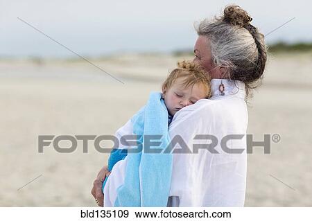 Stock Photo - Caucasian woman carrying grandson on beach. Fotosearch