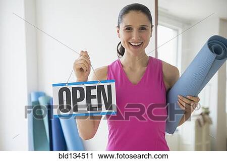 Stock Image - Caucasian woman holding open sign in yoga studio. Fotosearch
