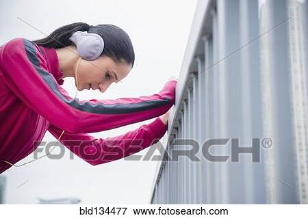 Stock Photo - Caucasian woman holding railing, listening to headphones. Fotosearch