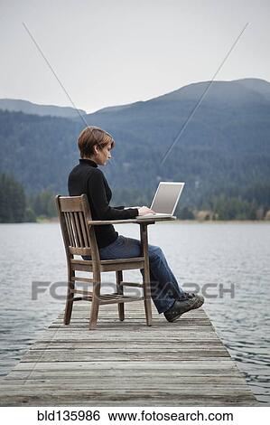 Caucasian woman using laptop on wooden dock on lake View Large Photo Image Stock Photograph - Caucasian woman using laptop on wooden dock on lake. Fotosearch