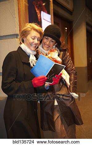 Picture - Caucasian women reading on city street at night. Fotosearch
